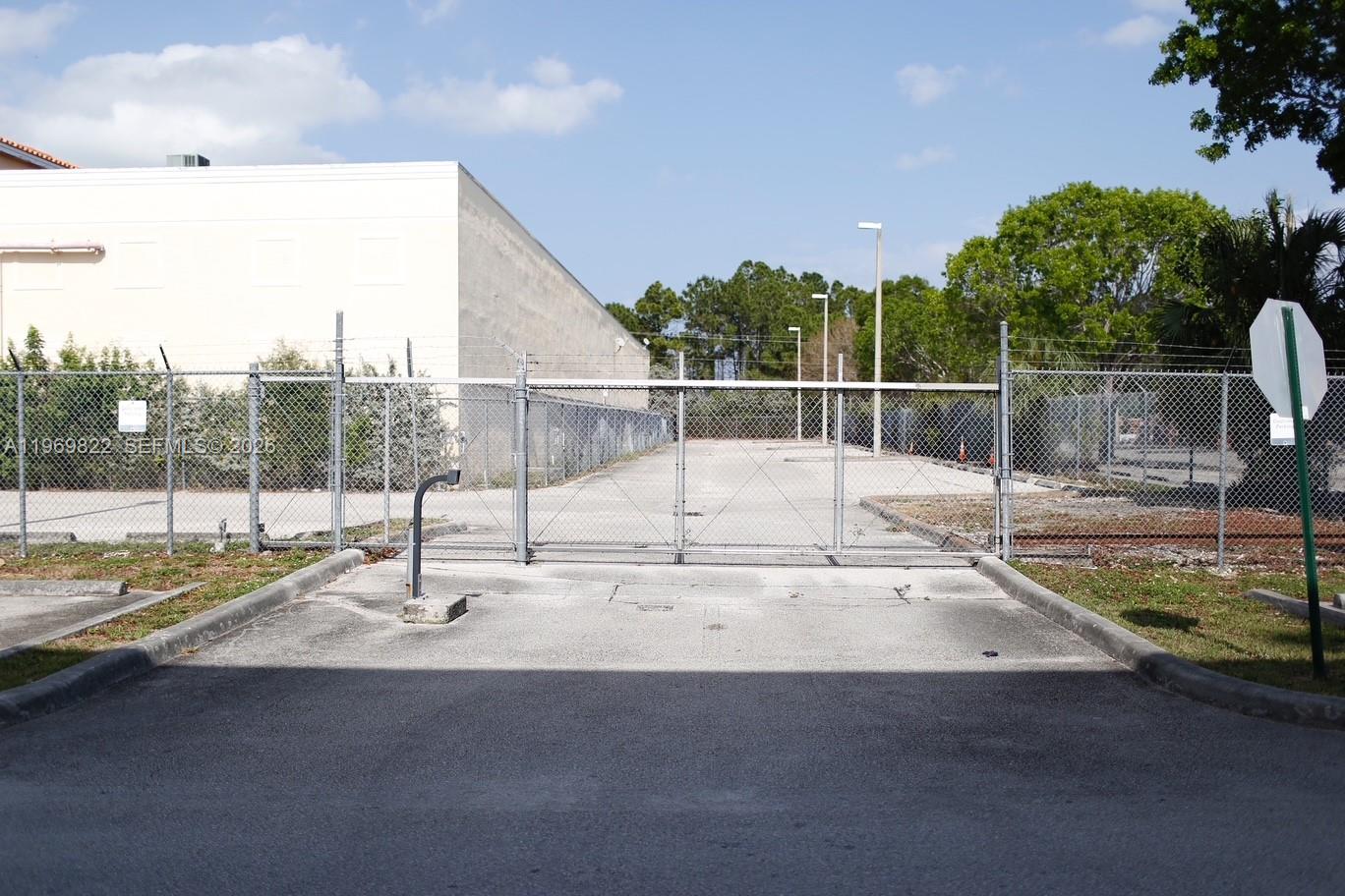 A gated chain-link fence secures a paved parking area next to a large commercial building — 12605 SW 134th Ct, Miami FL 33186, MIAMI, FL