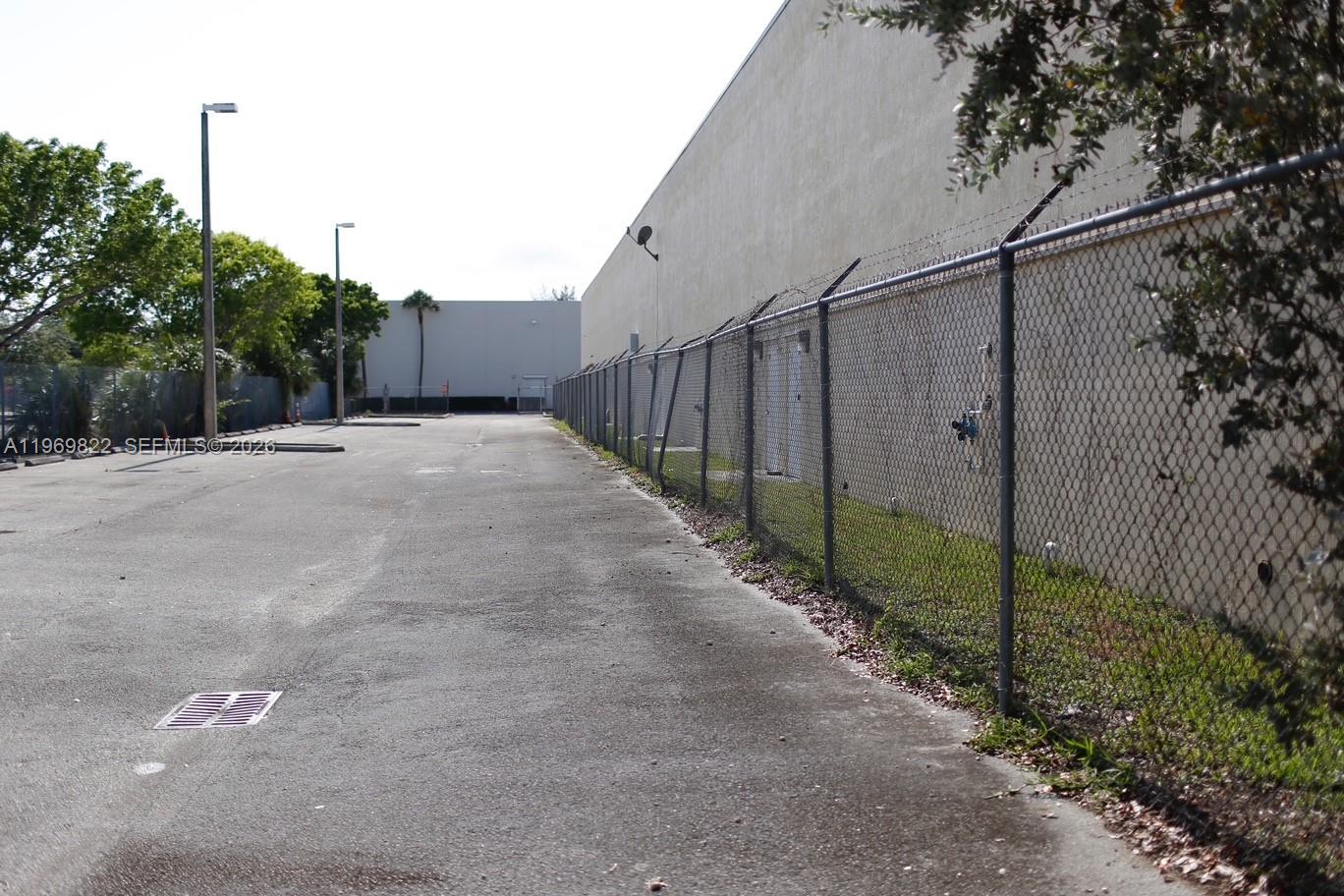 A paved outdoor area runs alongside a long building wall enclosed by a chain-link fence — 12605 SW 134th Ct, Miami FL 33186, MIAMI, FL