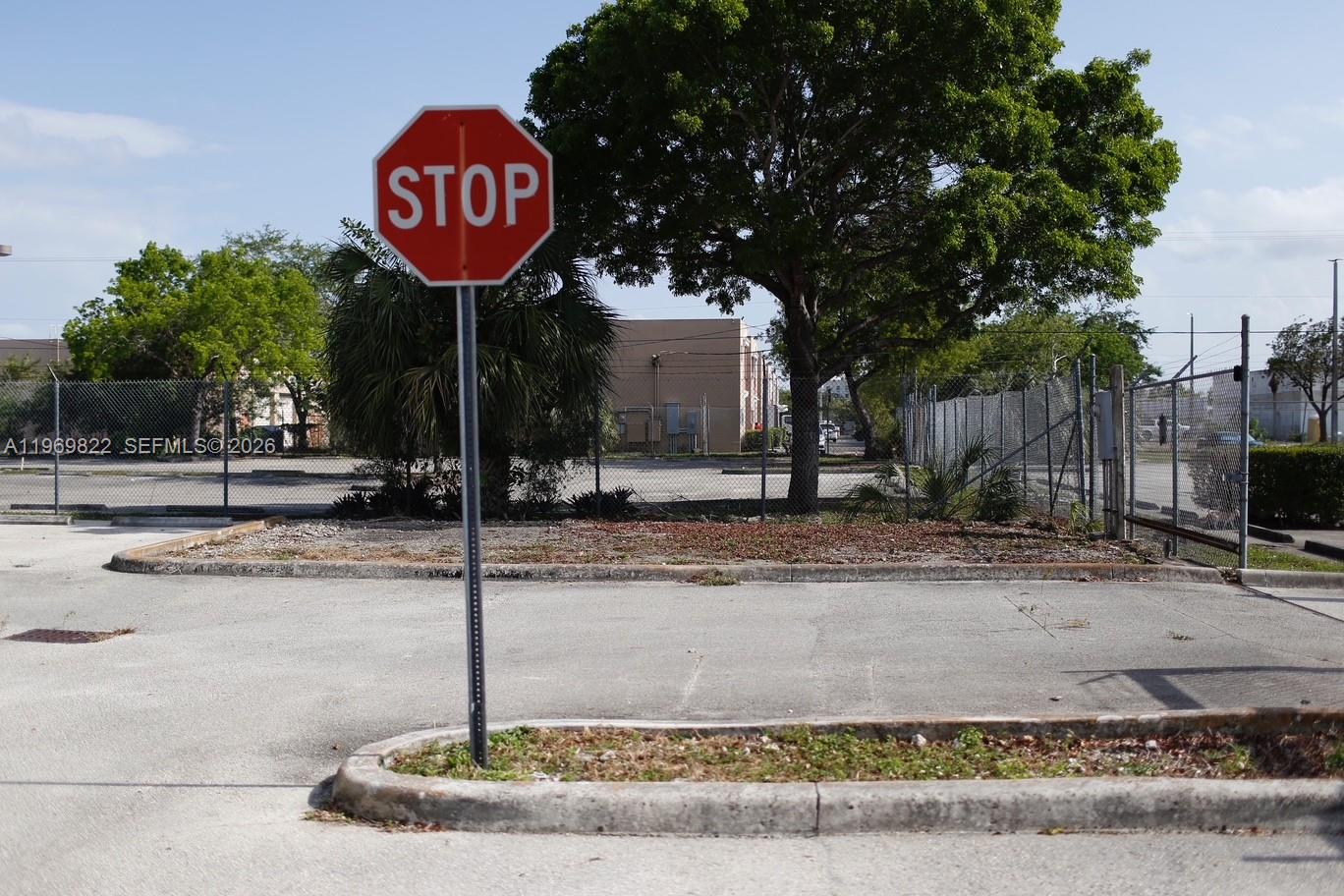 A stop sign stands in a paved parking lot near a chain-link fence and trees — 12605 SW 134th Ct, Miami FL 33186, MIAMI, FL