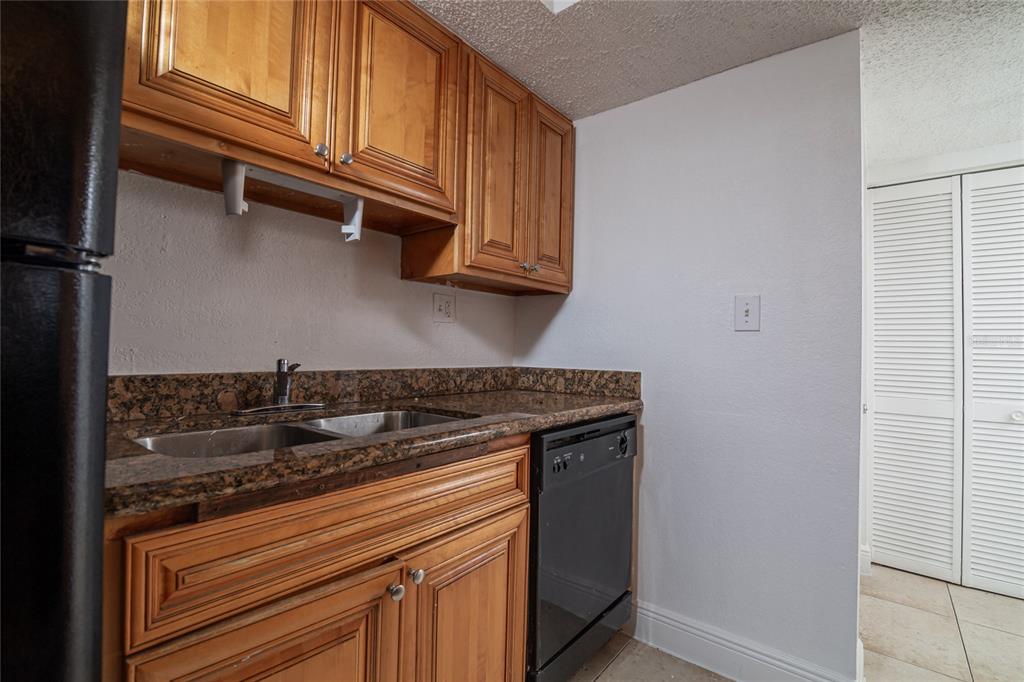 A kitchen features wood cabinets, granite countertops, a stainless steel sink, and a black dishwasher — 4789 S TEXAS AVENUE UNIT A, ORLANDO, FL
