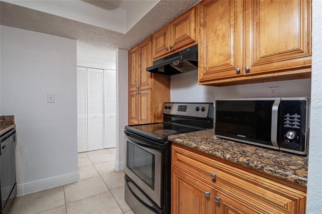 A kitchen features wood cabinets, granite countertops, a stainless steel stove, and a microwave — 4789 S TEXAS AVENUE UNIT A, ORLANDO, FL
