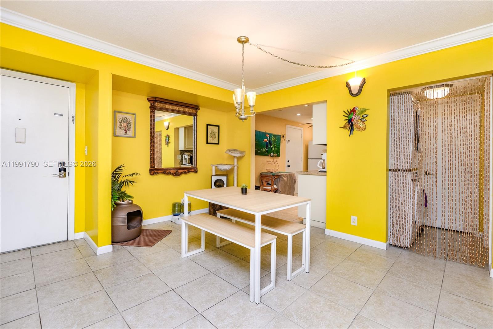A dining area features bright yellow walls, tile flooring, a wooden table with benches, and a mirror — 1428 SE 4th Ave # 240, Deerfield Beach FL 33441, DEERFIELD BEACH, FL