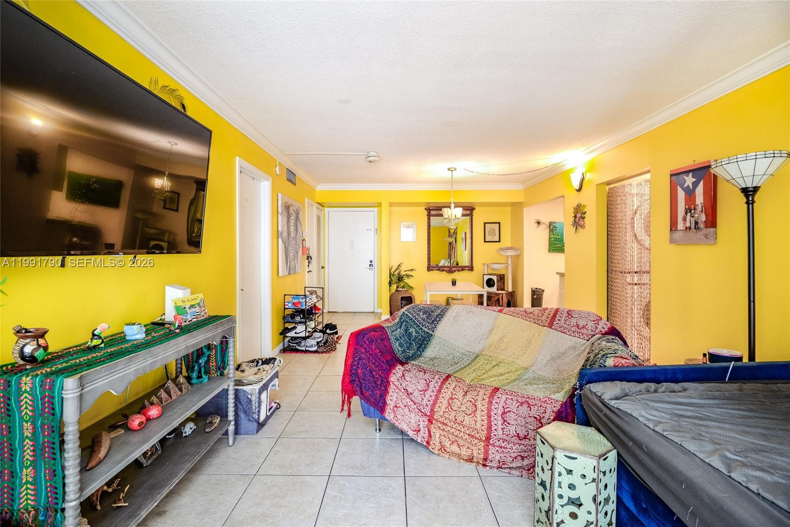 A living room with yellow walls, tile flooring, a television, and a patterned sofa — 1428 SE 4th Ave # 240, Deerfield Beach FL 33441, DEERFIELD BEACH, FL