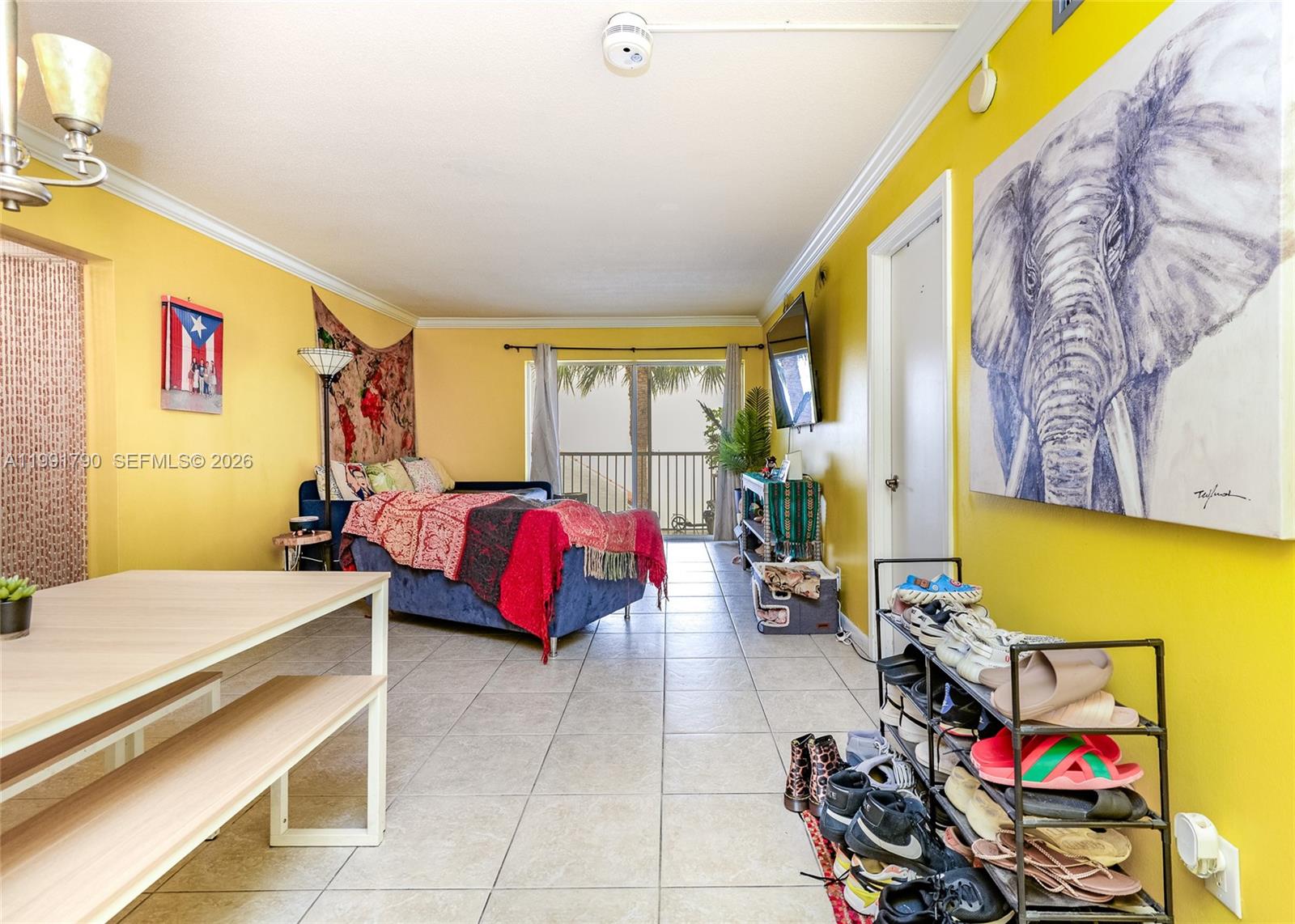 A living area with yellow walls, tile flooring, a blue sofa, and a shoe rack — 1428 SE 4th Ave # 240, Deerfield Beach FL 33441, DEERFIELD BEACH, FL
