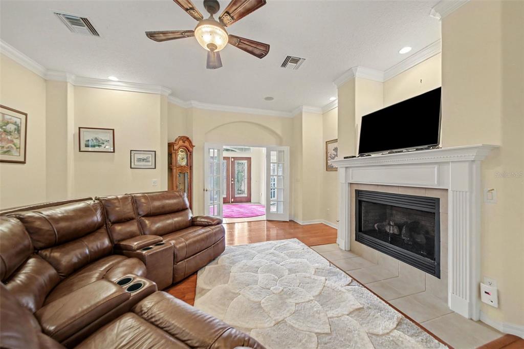 A living room features a brown leather sectional, a fireplace, and French doors leading outside — 5384 AURORA DRIVE, LEESBURG, FL