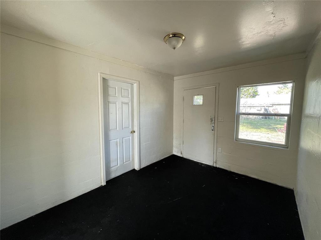 A room with white block walls, a white door, a window, and black carpeting — 131 B STREET UNIT 2, LAKE WALES, FL
