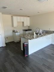 A kitchen features white cabinets, a granite countertop island, and dark wood-look flooring — 3199 DELTONA BOULEVARD, SPRING HILL, FL