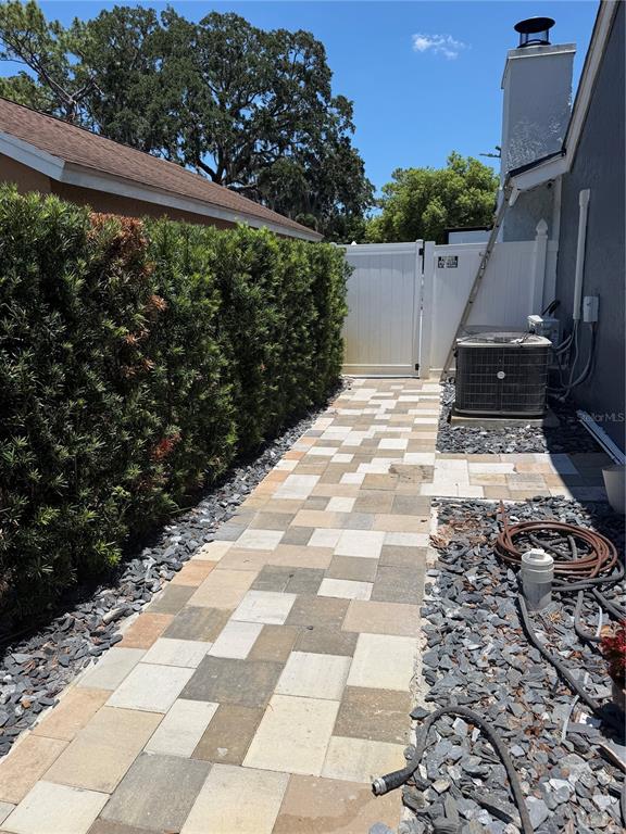 A paved walkway leads past a tall hedge toward a white gate and HVAC unit — 1409 PONCE DE LEON BOULEVARD, WINTER SPRINGS, FL