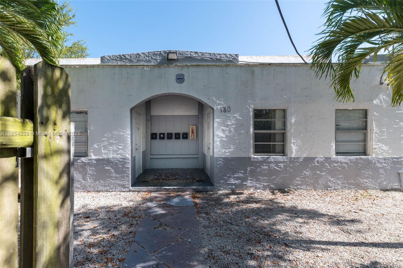 The exterior of a single-story building features a central arched entryway with mailboxes — 180 NW 59th St, Miami FL 33127, MIAMI, FL
