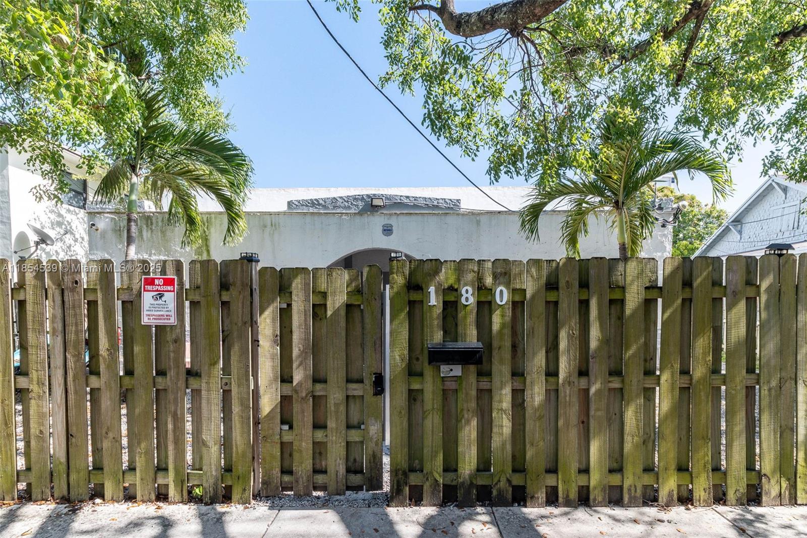 A wooden fence with a gate and house number 180 stands before a white building — 180 NW 59th St, Miami FL 33127, MIAMI, FL