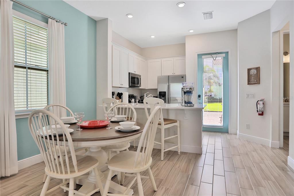 A dining area and kitchen feature white cabinets, a round wooden table, and light flooring — 8038 SURF STREET, KISSIMMEE, FL