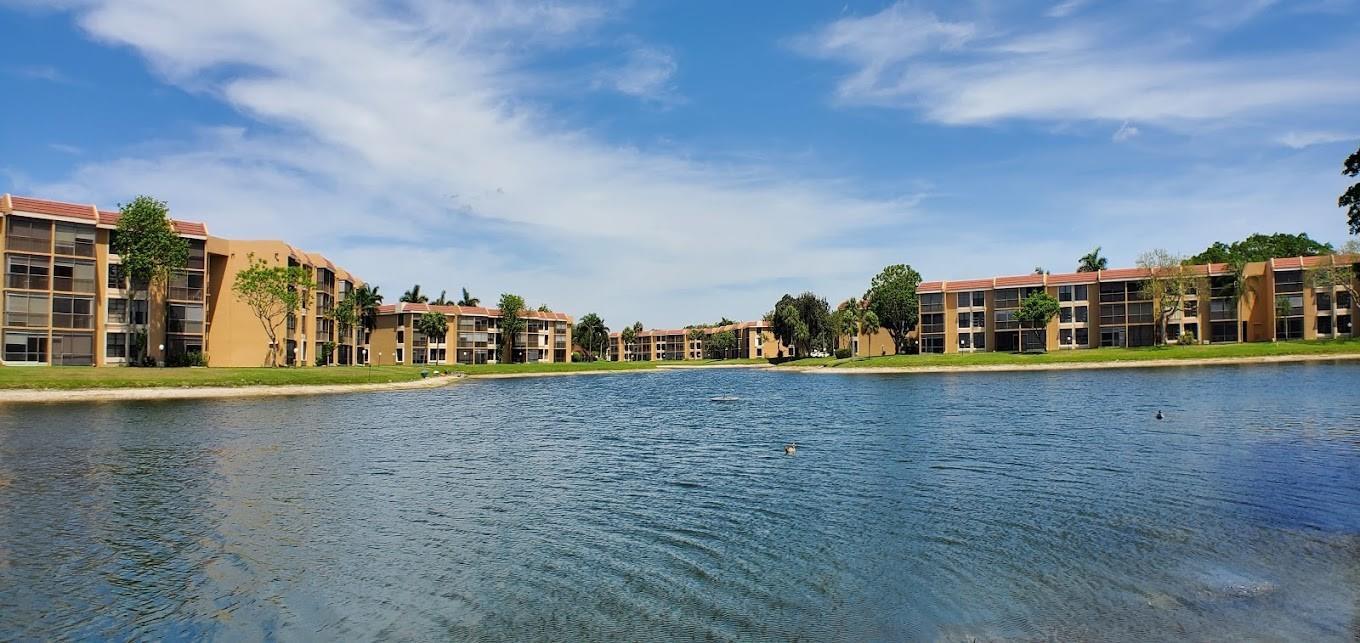 A multi-story apartment complex sits along the edge of a large, calm lake — 5609 Coral Lake # 109, Margate FL 33063, MARGATE, FL