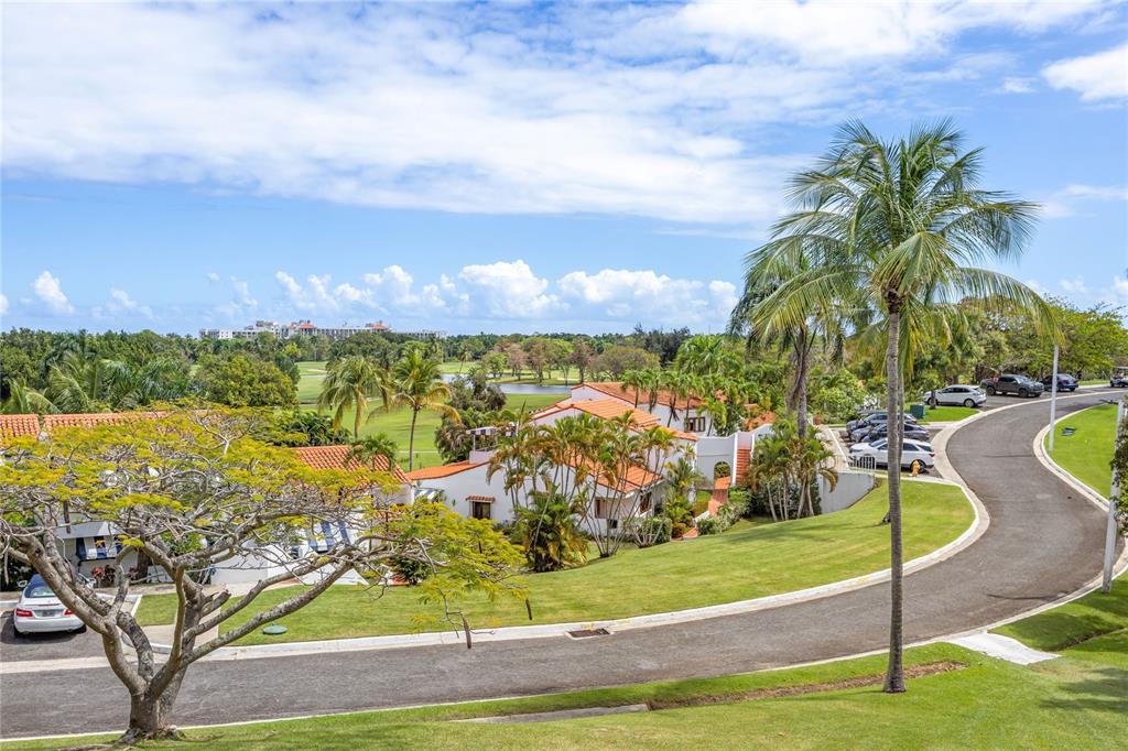 An elevated view shows a winding road, palm trees, and white buildings with orange roofs — RIO MAR CLUSTER 3, VILLA DEL AMANECER, RIO GRANDE, PR