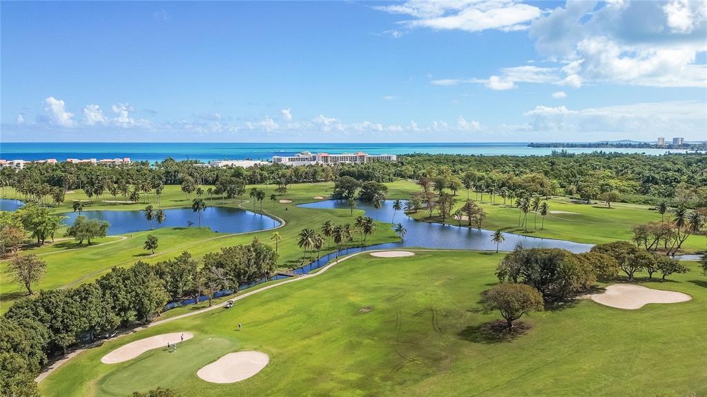 An aerial view of a golf course with ponds, palm trees, and a distant coastline — RIO MAR CLUSTER 3, VILLA DEL AMANECER, RIO GRANDE, PR