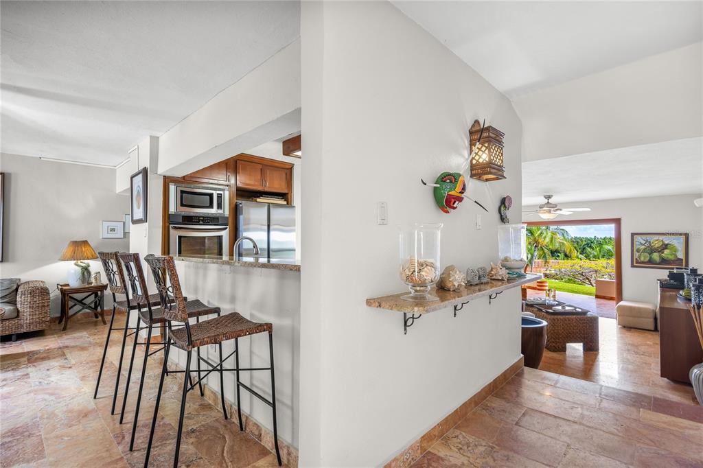 A kitchen with a breakfast bar and stone floors opens to a living area with views — RIO MAR CLUSTER 3, VILLA DEL AMANECER, RIO GRANDE, PR