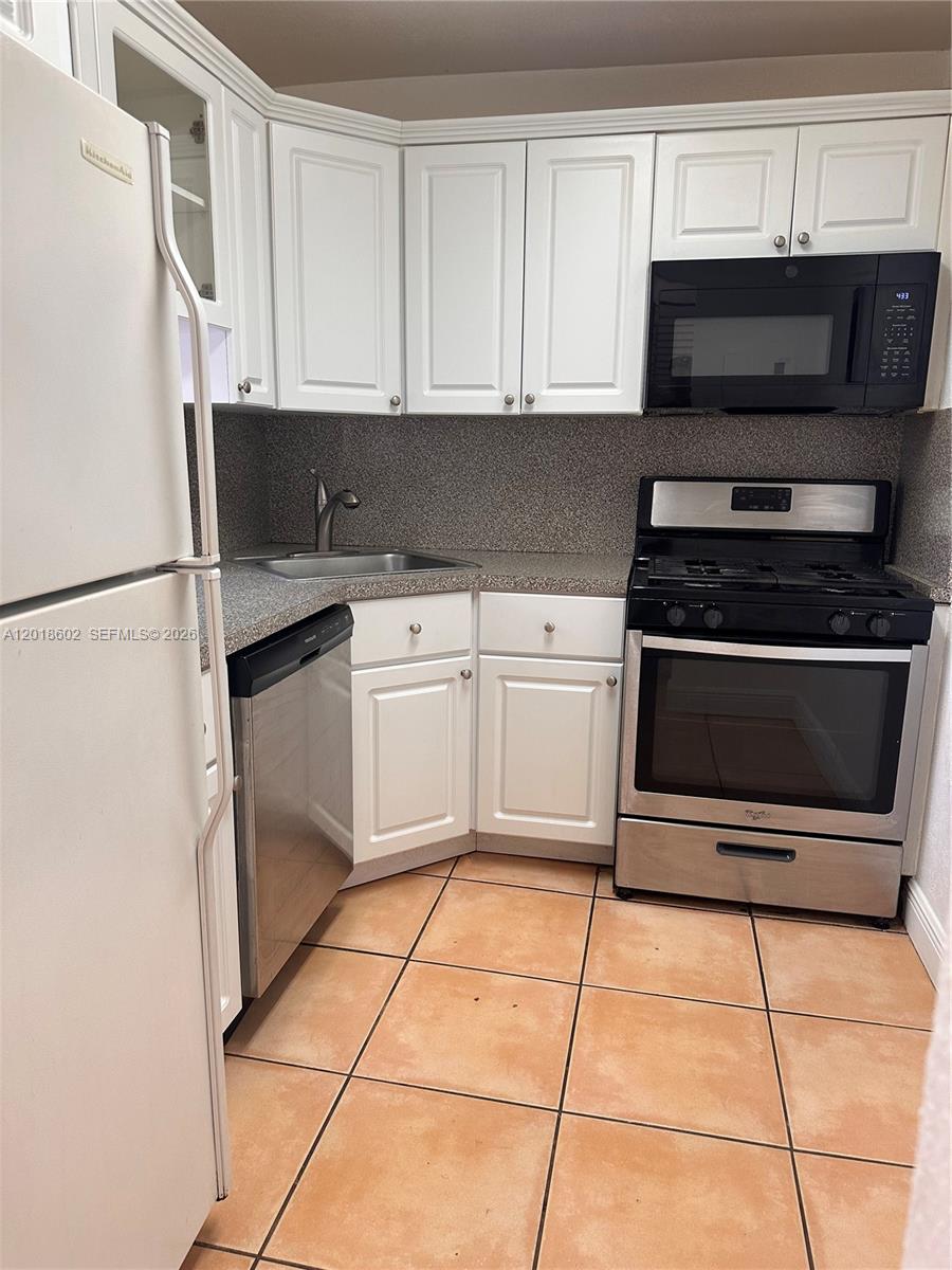 A small kitchen features white cabinets, stainless steel appliances, and tan floor tiles — 6713 N Kendall Dr # 611, Pinecrest FL 33156, PINECREST, FL