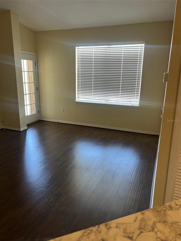 An empty room with dark wood-look flooring, a large window with blinds, and a door — 9122 MOONLIT MEADOWS LOOP UNIT 1, RIVERVIEW, FL