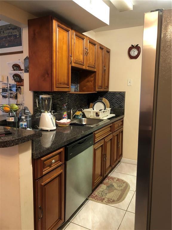 A kitchen features wood cabinets, dark granite countertops, a stainless steel dishwasher, and tiled floors — LAUDERHILL, FL