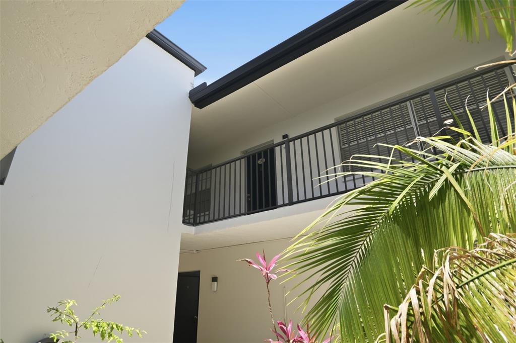 A low-angle view of a two-story building exterior with a black metal balcony railing — 1127 KING ARTHUR COURT UNIT 316, DUNEDIN, FL