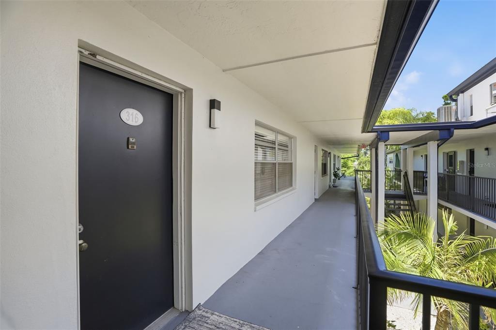 An exterior apartment walkway features a dark door numbered 316 and a metal railing — 1127 KING ARTHUR COURT UNIT 316, DUNEDIN, FL
