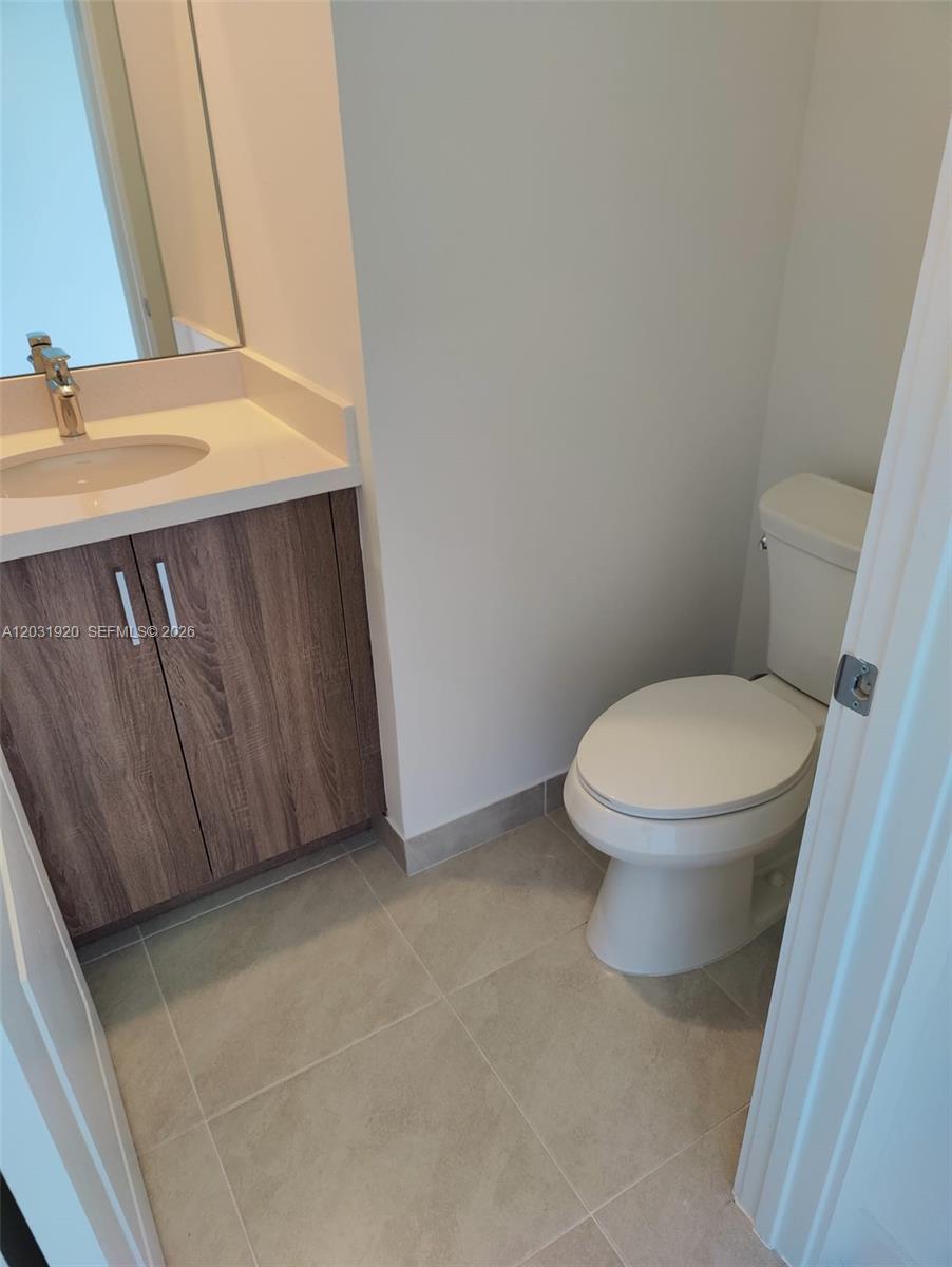 A small bathroom features a wood-grain vanity, white countertop, and a white toilet — 5573 Cobalto Way # 5573, Ave Maria FL 34142, AVE MARIA, FL