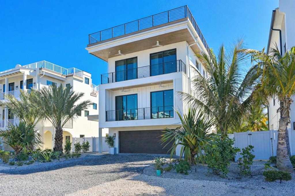 A modern three-story white house with balconies and a gravel driveway under a blue sky — 111 PALMETTO AVENUE, ANNA MARIA, FL