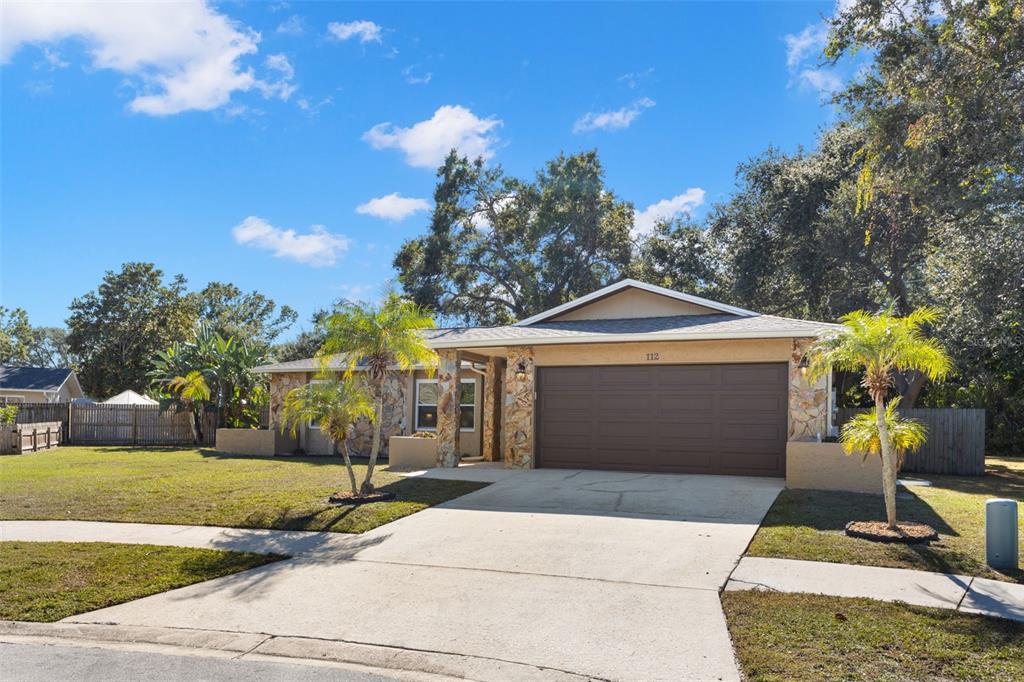 A single-story house with stone siding, a brown garage door, and palm trees in front — 112 MEADOWCROSS DRIVE, SAFETY HARBOR, FL