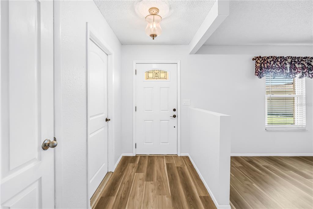 A bright entryway features white walls, wood-look flooring, a white front door, and a ceiling light — 112 MEADOWCROSS DRIVE, SAFETY HARBOR, FL