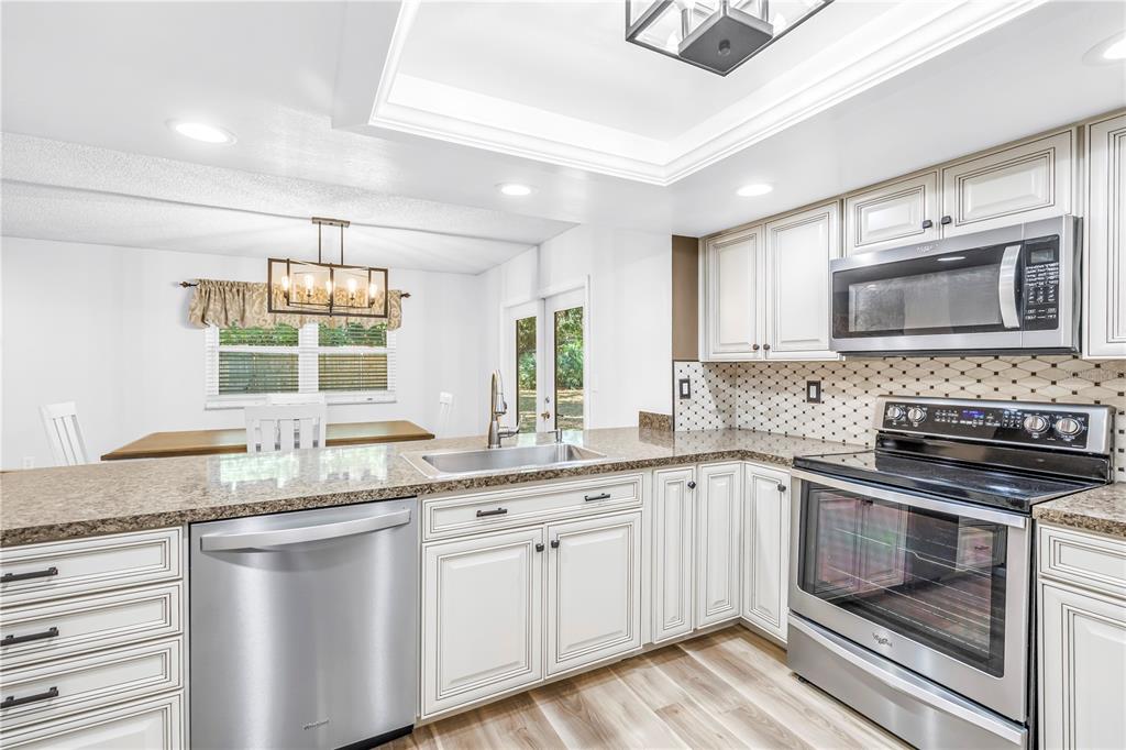A kitchen features white cabinets, granite countertops, stainless steel appliances, and an adjacent dining area — 112 MEADOWCROSS DRIVE, SAFETY HARBOR, FL