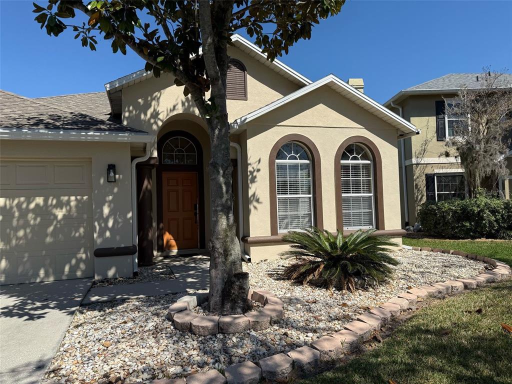A tan stucco house features an arched entryway, two arched windows, and a rock garden — 2227 OAKINGTON STREET, WINTER GARDEN, FL