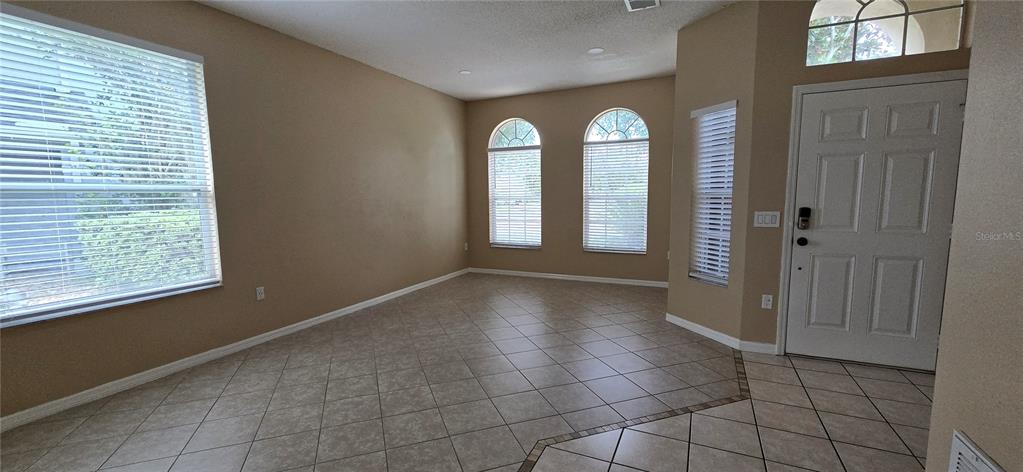 An empty room features beige walls, tiled floors, several windows with blinds, and a front door — 2227 OAKINGTON STREET, WINTER GARDEN, FL