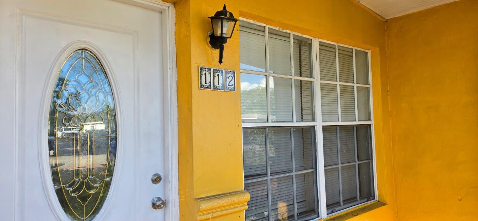 A yellow exterior wall features a white front door, a window, and house number 112 — 112 Newton Road, West Park FL 33023, WEST PARK, FL