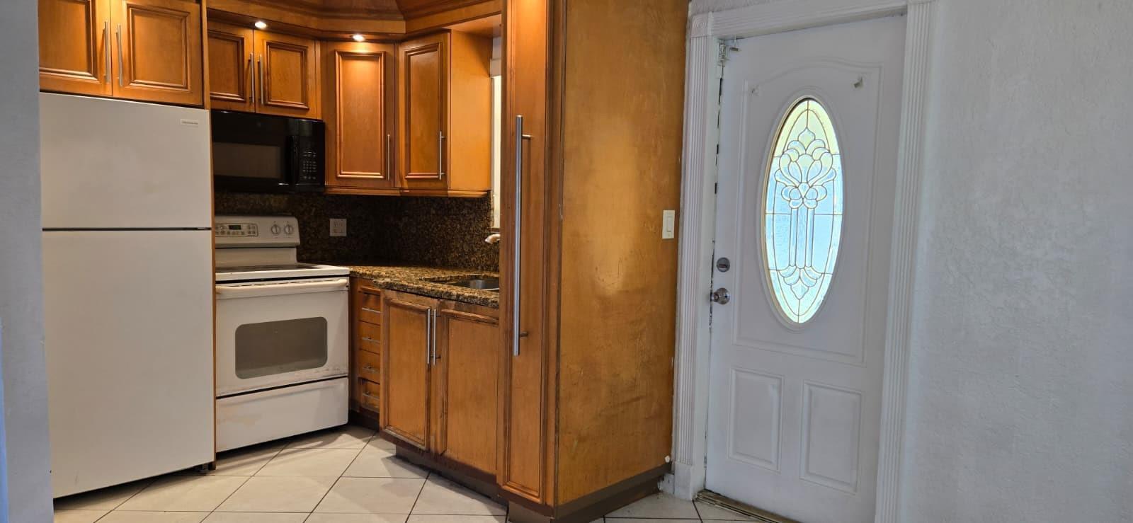 A kitchen with wood cabinets, granite countertops, and a white refrigerator next to a door — 112 Newton Road, West Park FL 33023, WEST PARK, FL