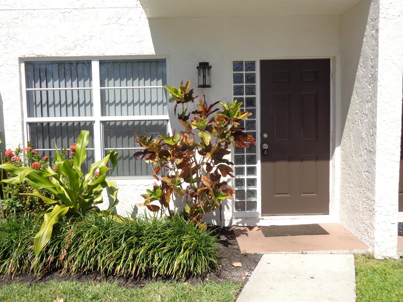 The exterior of a white stucco home features a brown front door and landscaping — 1917 NE 3rd Street # 103, Deerfield Beach FL 33441, DEERFIELD BEACH, FL