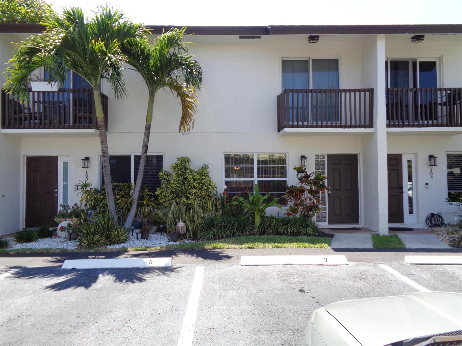 The exterior of a two-story apartment building features brown doors, balconies, and a parking lot — 1917 NE 3rd Street # 103, Deerfield Beach FL 33441, DEERFIELD BEACH, FL