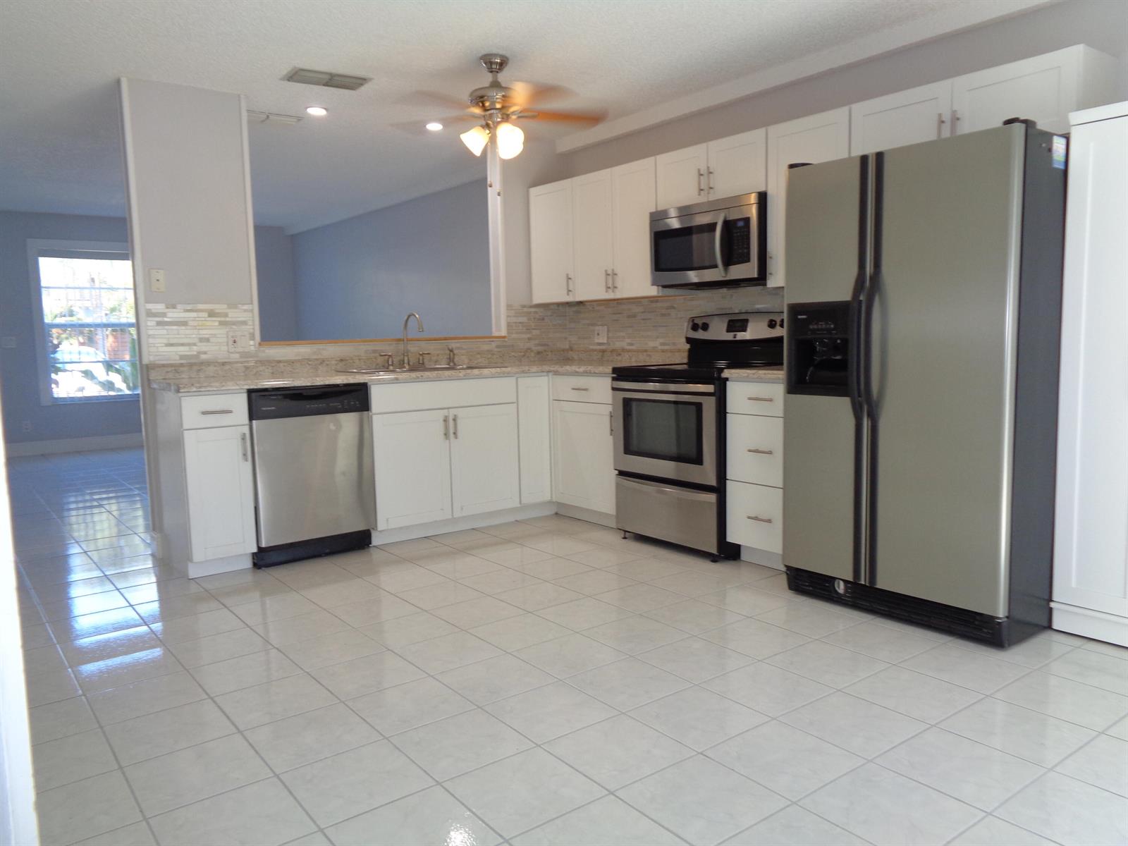 A kitchen features white cabinets, stainless steel appliances, granite countertops, and light-colored tile flooring — 1917 NE 3rd Street # 103, Deerfield Beach FL 33441, DEERFIELD BEACH, FL