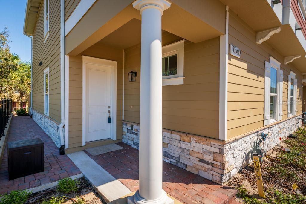 A tan house exterior features a white door, a stone base, and a white column — 7549 SUNFLOWER CIRCLE, KISSIMMEE, FL