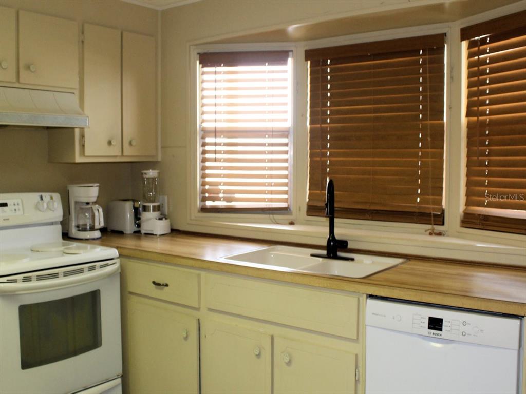 A kitchen features white cabinets, a wood-look countertop, a white stove, and a window sink — 476 NEEDLE PALM STREET, LARGO, FL