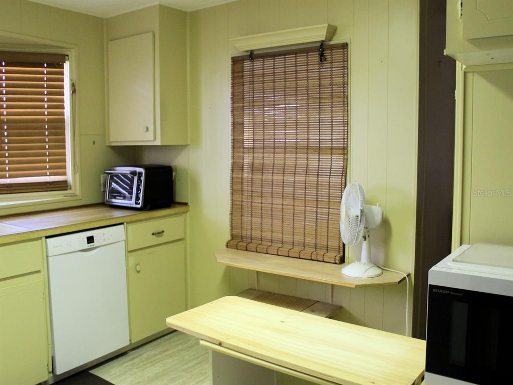 A kitchen features light green cabinets, a white dishwasher, a microwave, and a wooden table — 476 NEEDLE PALM STREET, LARGO, FL