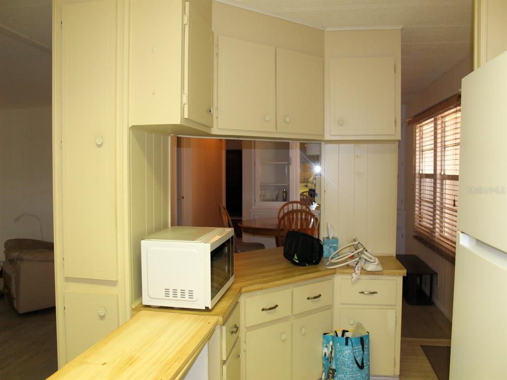 A kitchen with light-colored cabinets, a microwave, and a wooden countertop overlooking a dining area — 476 NEEDLE PALM STREET, LARGO, FL