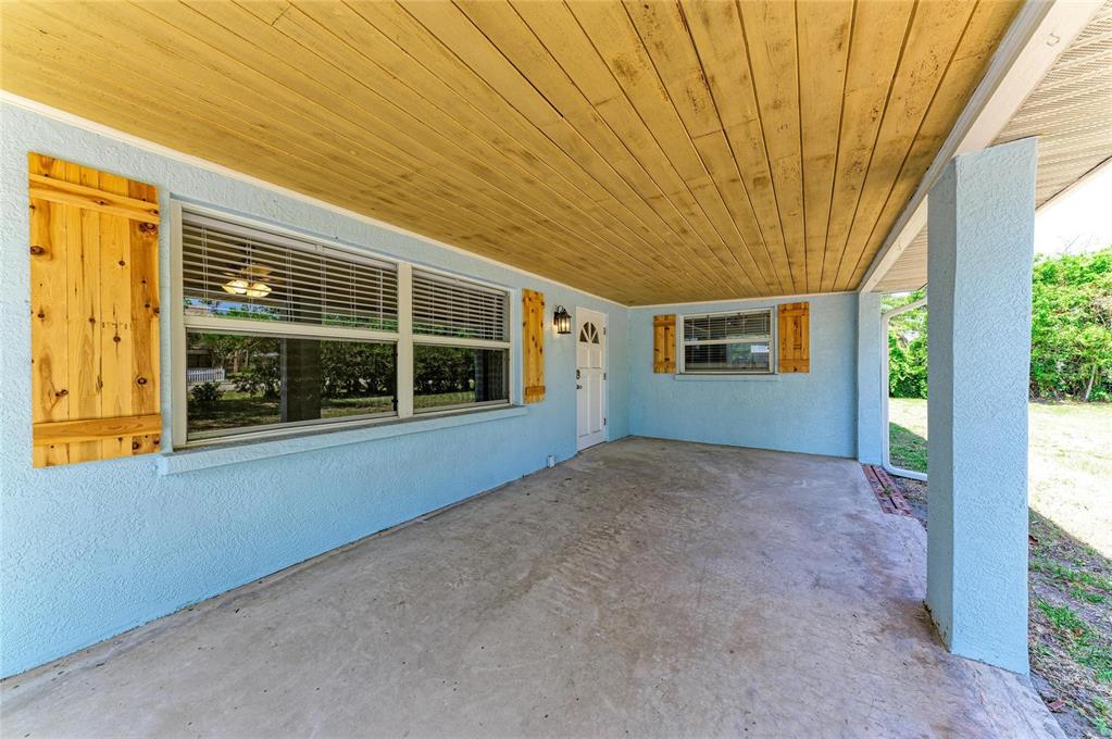A covered concrete porch features light blue stucco walls, wood-plank ceilings, and rustic wooden shutters — 2401 10TH STREET W, PALMETTO, FL