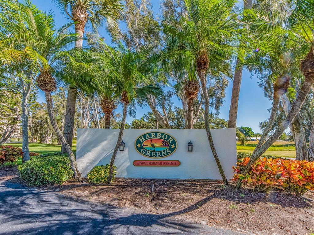 A white stucco sign for Harbor Greens stands surrounded by palm trees and landscaping — 9490 HARBOR GREENS WAY UNIT 305, SEMINOLE, FL