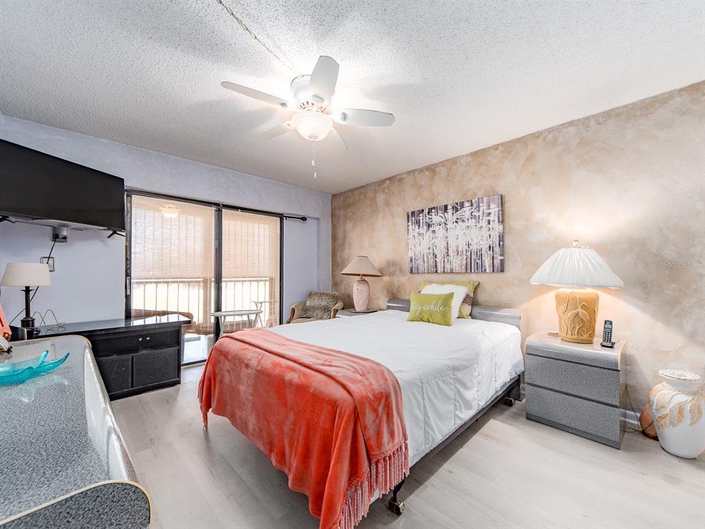 A bedroom features a bed with a coral throw, a ceiling fan, and textured walls — 9490 HARBOR GREENS WAY UNIT 305, SEMINOLE, FL