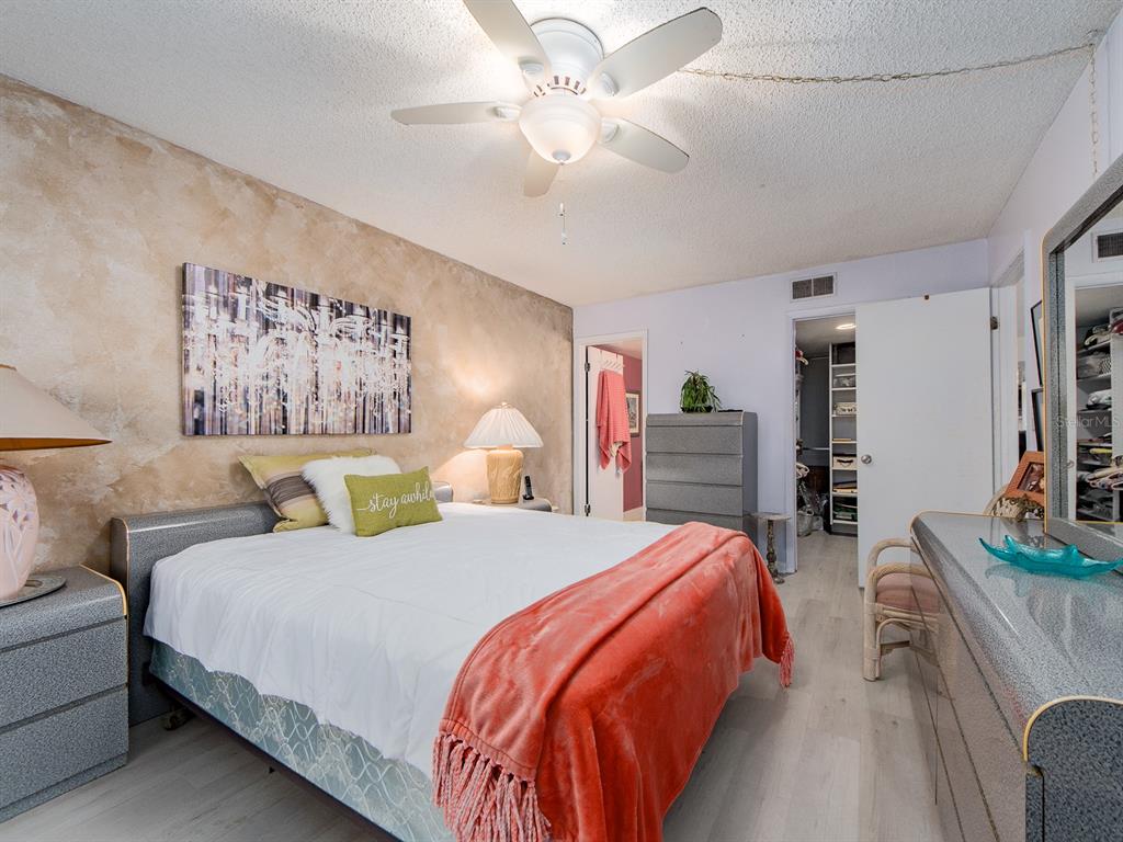 A bedroom features a bed with a coral throw, textured accent wall, and ceiling fan — 9490 HARBOR GREENS WAY UNIT 305, SEMINOLE, FL
