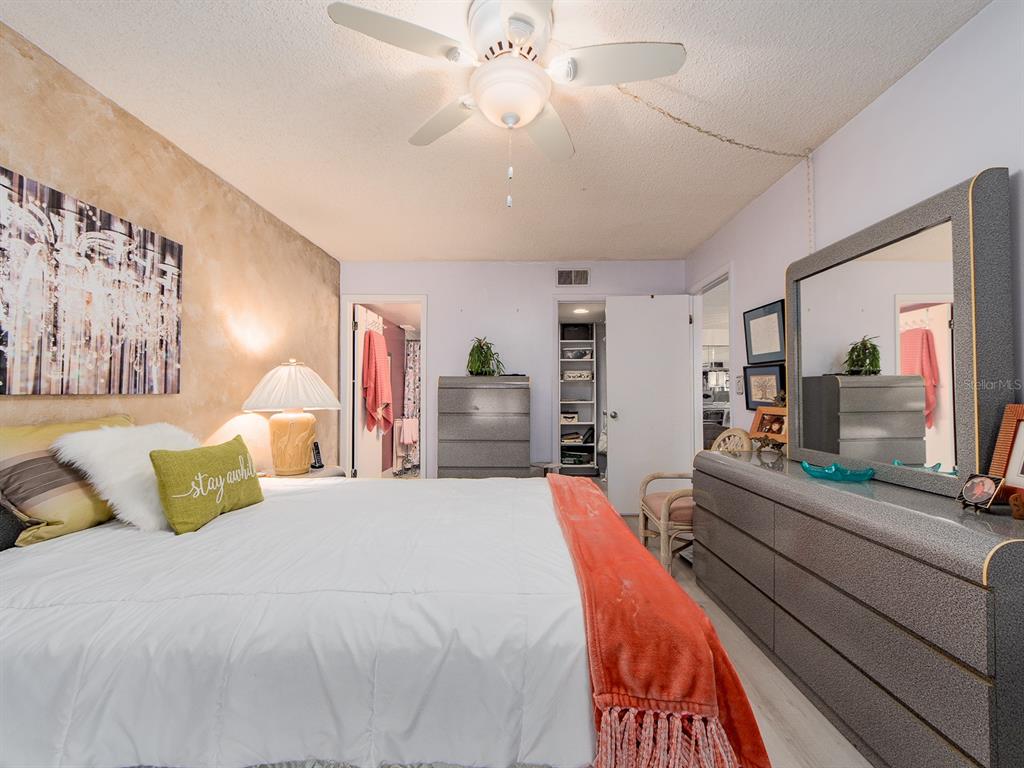 A bedroom features a bed with a white comforter, a dresser with a mirror, and ceiling fan — 9490 HARBOR GREENS WAY UNIT 305, SEMINOLE, FL