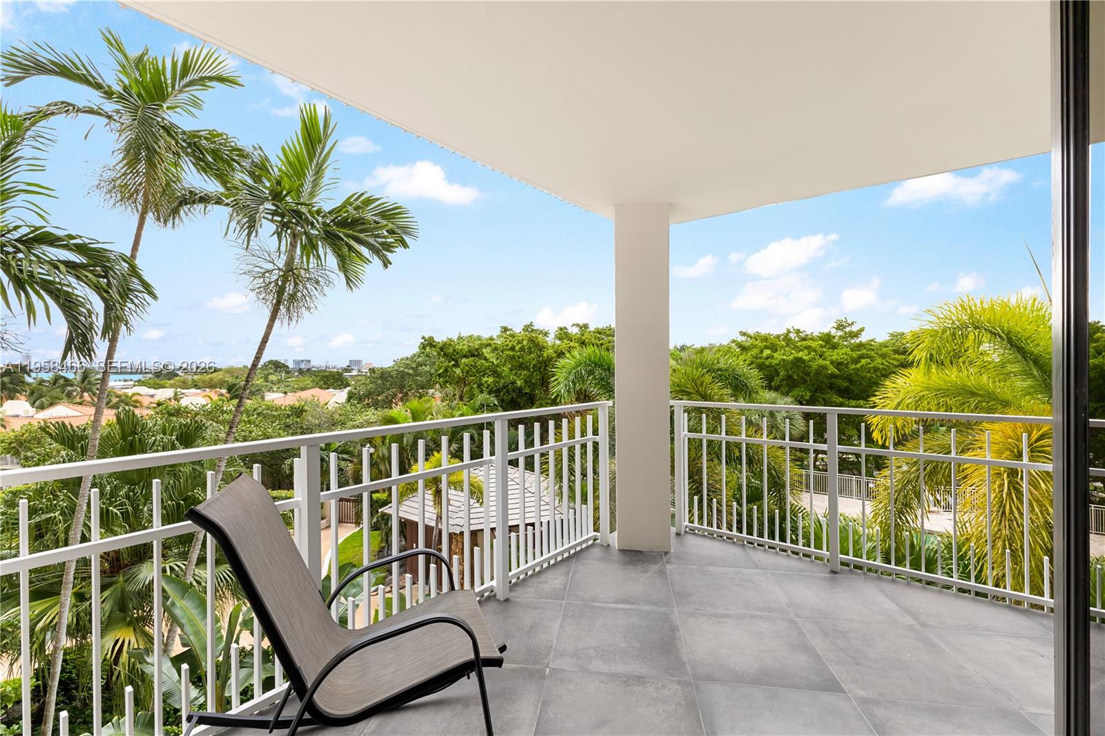 A covered balcony features gray tile flooring, a white metal railing, and a lounge chair — 1000 Quayside Ter # 506, Miami FL 33138, MIAMI, FL