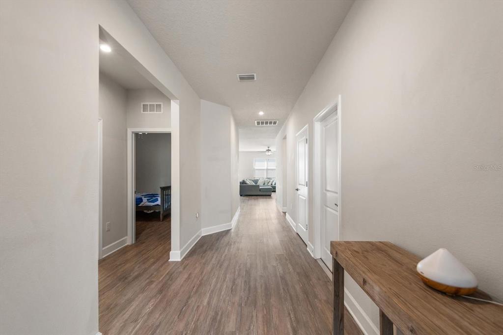 A hallway with wood-look flooring leads to a living area with two doors on the right — 12353 BLUE PACIFIC DRIVE, RIVERVIEW, FL