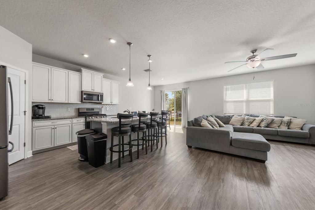An open-concept kitchen and living area features white cabinets, a kitchen island, and gray flooring — 12353 BLUE PACIFIC DRIVE, RIVERVIEW, FL