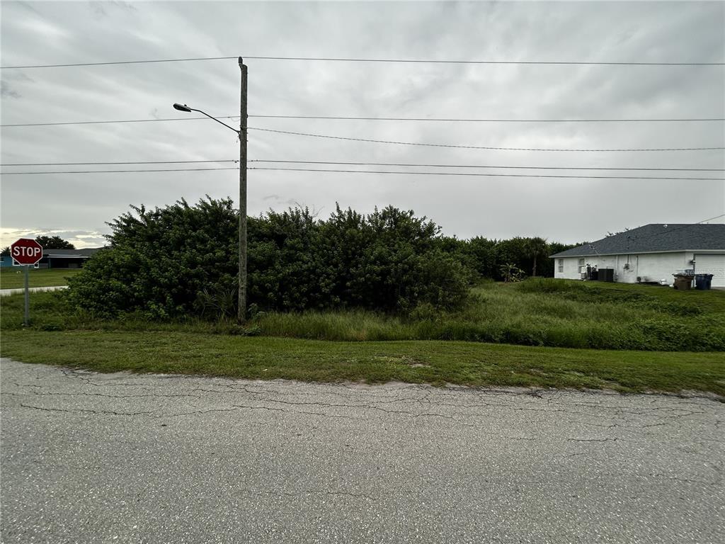 A vacant, overgrown lot sits between a residential house and a street with a stop sign — 165 PEMBROKE STREET, LEHIGH ACRES, FL