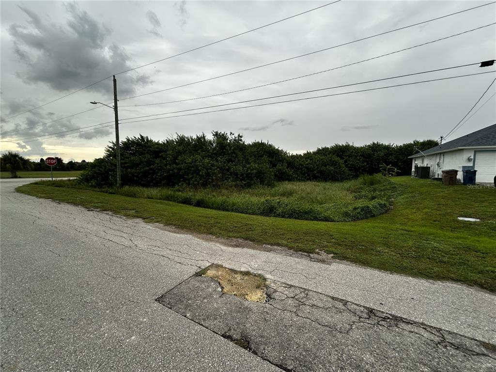 A vacant, grass-covered corner lot sits next to a house under a cloudy sky — 165 PEMBROKE STREET, LEHIGH ACRES, FL